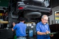 Senior foreman checking list of vehicle repair service while two mechanic checking wheel, inspecting under car body of customer Royalty Free Stock Photo