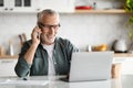 Senior Freelancer Man Working With Laptop And Talking On Cellphone At Home Royalty Free Stock Photo