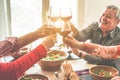 Senior friends cheering with wine glasses at home lunch - Happy mature people having fun together - Focus on left bottom glass - Royalty Free Stock Photo