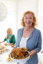 Senior woman serving roasted chicken for Thanksgiving dinner with friends