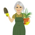 Senior gardening woman holding green Chlorophytum plant in the pot and trowel Royalty Free Stock Photo