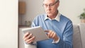 Senior Gentleman Using Tablet Sitting On Sofa At Home, Panorama