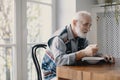 Senior grandfather with grey hair and beard sitting alone in the kitchen eating breakfast