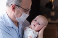 Grandfather in medical mask holding a caucasian newborn baby girl in his hands Royalty Free Stock Photo