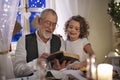 Senior grandfather with small granddaughter indoors at Christmas, reading Bible.