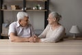 Senior grandparents sit at table holding hands feeling love