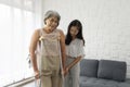 Senior gray hair woman exercise and practice walking at home. Young asian woman help her grandma walk by using axilla crutches