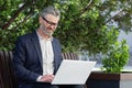 Senior gray haired boss working on laptop outside office building outdoors, mature businessman typing on keyboard Royalty Free Stock Photo