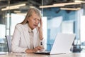 Senior gray-haired businesswoman working in the office, sitting at the desk, holding her head with her hand and Royalty Free Stock Photo