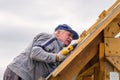 Senior builder man with a screwdriver screwing a roofing sheet to the roof