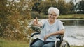 Senior gray haired lady in the wheelchair neear the river showing thumbs up Royalty Free Stock Photo