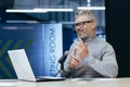 Senior man sitting an office with a microphone in front of a laptop. Talks on a video call