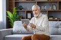 Senior gray-haired man sitting on the sofa at home, using a tablet, talking on a video call and looking at the camera Royalty Free Stock Photo