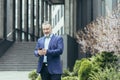 Senior gray-haired man in a suit, stands near the office center and calls a taxi from the phone Royalty Free Stock Photo