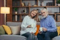 Senior gray-haired married couple man and woman at home together, relaxing together in the evening, sitting on the couch and Royalty Free Stock Photo