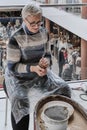 Senior gray-haired woman kneading clay in her hands to sculpt clay vase on potter& x27;s wheel. Royalty Free Stock Photo