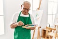 Senior grey-haired artist man smiling happy painting at art studio