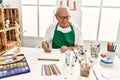 Senior grey-haired artist man smiling happy painting sitting on the table at art studio Royalty Free Stock Photo