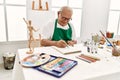 Senior grey-haired artist man smiling happy painting sitting on the table at art studio Royalty Free Stock Photo