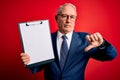 Senior grey haired business man holding clipboard over red background with angry face, negative sign showing dislike with thumbs Royalty Free Stock Photo