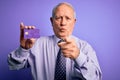 Senior grey haired business man holding credit card over purple background pointing with finger to the camera and to you, hand Royalty Free Stock Photo