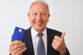 Senior grey-haired businessman holding credit card over isolated white background pointing and showing with thumb up to the side Royalty Free Stock Photo