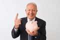 Senior grey-haired businessman holding piggy bank standing over isolated white background surprised with an idea or question Royalty Free Stock Photo