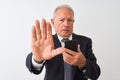 Senior grey-haired businessman using smartphone standing over isolated white background with open hand doing stop sign with Royalty Free Stock Photo