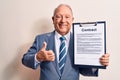 Senior grey-haired businessman wearing suit holding clipboard with contract document smiling happy and positive, thumb up doing Royalty Free Stock Photo