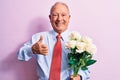 Senior grey-haired businessman wearing tie holding bouquet of flowers over pink background smiling happy and positive, thumb up Royalty Free Stock Photo