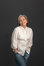 Senior grey haired charming woman looking happy wearing white shirt and denim jeans on camera isolated on grey