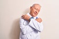 Senior grey-haired doctor man wearing coat and stethoscope standing over white background hugging oneself happy and positive, Royalty Free Stock Photo