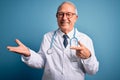 Senior grey haired doctor man wearing stethoscope and medical coat over blue background amazed and smiling to the camera while Royalty Free Stock Photo