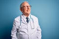 Senior grey haired doctor man wearing stethoscope and medical coat over blue background looking away to side with smile on face, Royalty Free Stock Photo