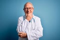 Senior grey haired doctor man wearing stethoscope and medical coat over blue background looking confident at the camera smiling Royalty Free Stock Photo