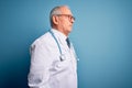 Senior grey haired doctor man wearing stethoscope and medical coat over blue background looking to side, relax profile pose with Royalty Free Stock Photo