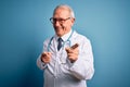 Senior grey haired doctor man wearing stethoscope and medical coat over blue background pointing fingers to camera with happy and Royalty Free Stock Photo