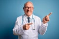 Senior grey haired doctor man wearing stethoscope and medical coat over blue background smiling and looking at the camera pointing Royalty Free Stock Photo