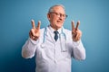 Senior grey haired doctor man wearing stethoscope and medical coat over blue background smiling looking to the camera showing Royalty Free Stock Photo
