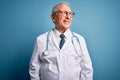 Senior grey haired doctor man wearing stethoscope and medical coat over blue background smiling looking to the side and staring Royalty Free Stock Photo