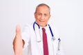 Senior grey-haired doctor man wearing stethoscope standing over isolated white background smiling friendly offering handshake as Royalty Free Stock Photo