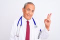 Senior grey-haired doctor man wearing stethoscope standing over isolated white background smiling with happy face winking at the Royalty Free Stock Photo