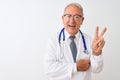 Senior grey-haired doctor man wearing stethoscope standing over isolated white background smiling with happy face winking at the Royalty Free Stock Photo