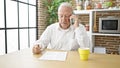 Senior grey-haired man angry arguing on smartphone sitting on table at dinning room