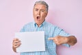 Senior grey-haired man holding blank empty banner angry and mad screaming frustrated and furious, shouting with anger