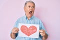 Senior grey-haired man holding heart draw angry and mad screaming frustrated and furious, shouting with anger looking up Royalty Free Stock Photo