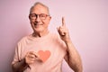 Senior grey haired man holding heart shape paper over pink background surprised with an idea or question pointing finger with Royalty Free Stock Photo