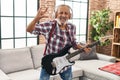 Senior grey-haired man playing electrical guitar doing horns symbol with hand at home Royalty Free Stock Photo