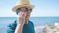 Senior grey-haired man tourist wearing summer hat talking on smartphone at seaside Royalty Free Stock Photo