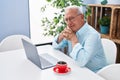 Senior grey-haired man using laptop and drinking coffee sitting on table at home Royalty Free Stock Photo